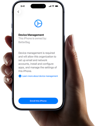 En persons højre hånd holder en iPhone med tekst på skærmen, der forklarer, hvad Administration af enhed er, og viser en mulighed for tilmelding