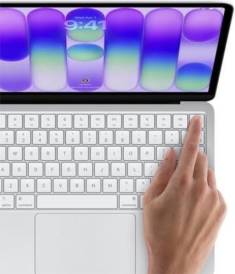 MacBook Neo, hopeanvärinen, esillä kirjautumisnäyttö, henkilön sormi Touch ID ‑tunnistimella näppäimistön oikeassa yläkulmassa